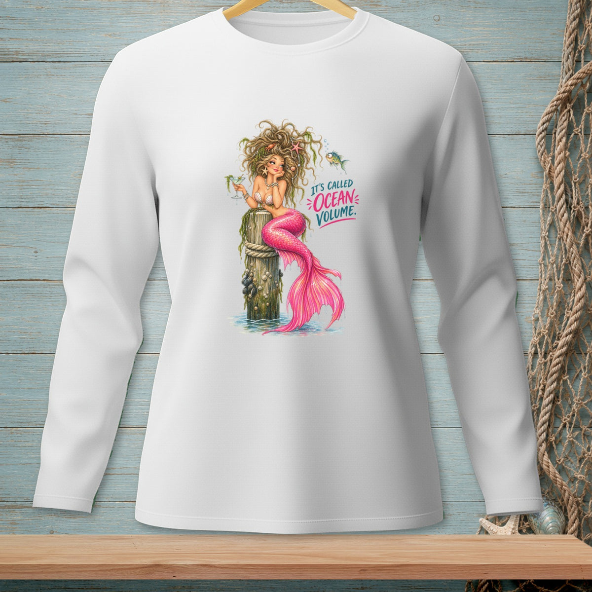 White long-sleeve shirt with a mermaid sitting on a post, text "IT'S CALLED OCEAN VOLUME."
