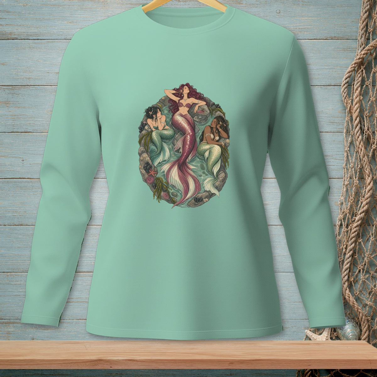 Mint green long-sleeve shirt with a circular graphic of three mermaids in a reef setting.