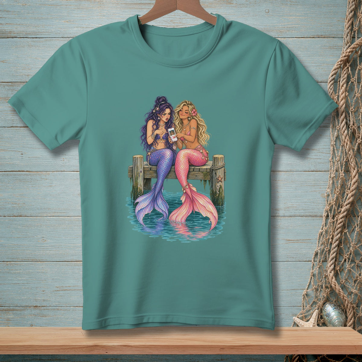 Two mermaids sit on a dock looking at a smartphone.