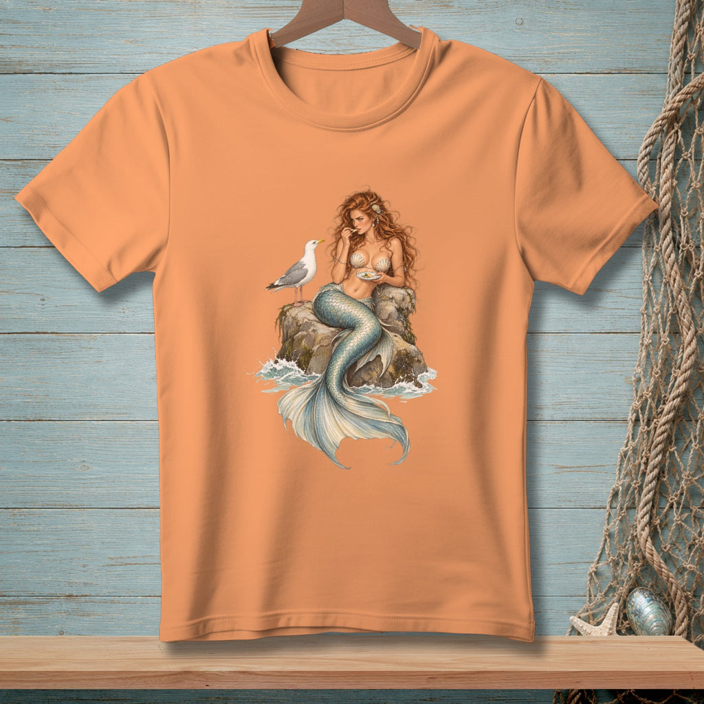 Orange t-shirt with a detailed illustration of a mermaid and seagull on a rock.