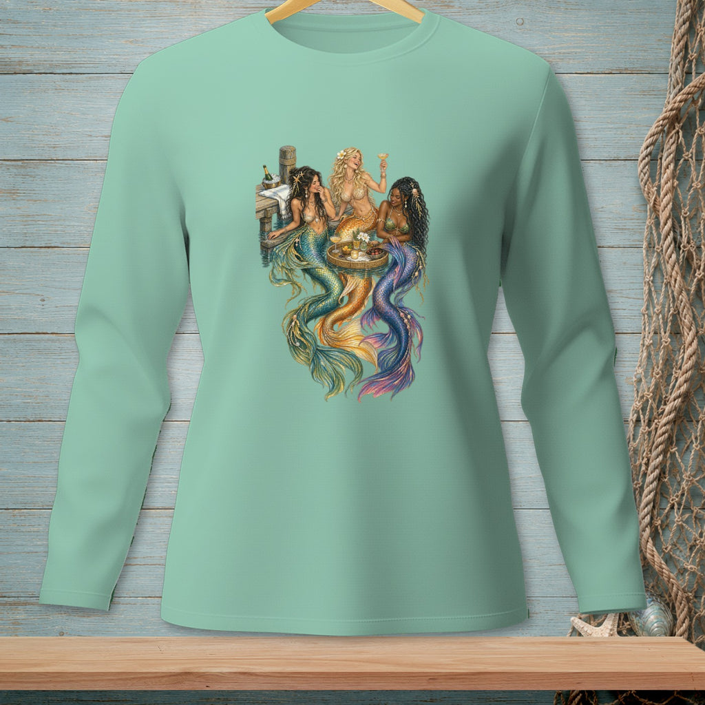 Three mermaids with colorful tails gather around a table with drinks.