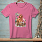 Pink t-shirt with a mermaid lounging on a rock with a seagull and a plate of food.