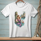 White t-shirt featuring a watercolor illustration of a mermaid by a pier with a crab and shops.