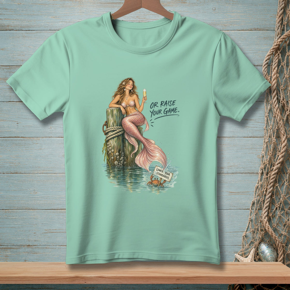 Mint t-shirt with mermaid on post and crab holding sign saying "Lower Your Standards."