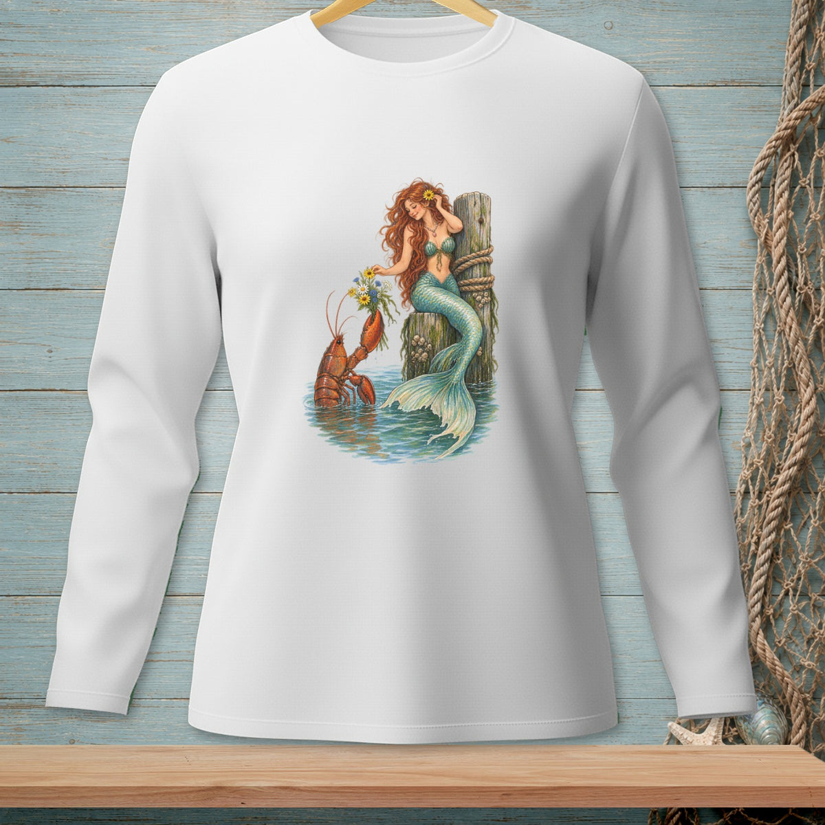 White long-sleeve shirt with a watercolor print of a mermaid and lobster by a dock.