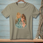 Two mermaids, one blonde with a teal tail and one brunette with a coral tail, sit on a dock.