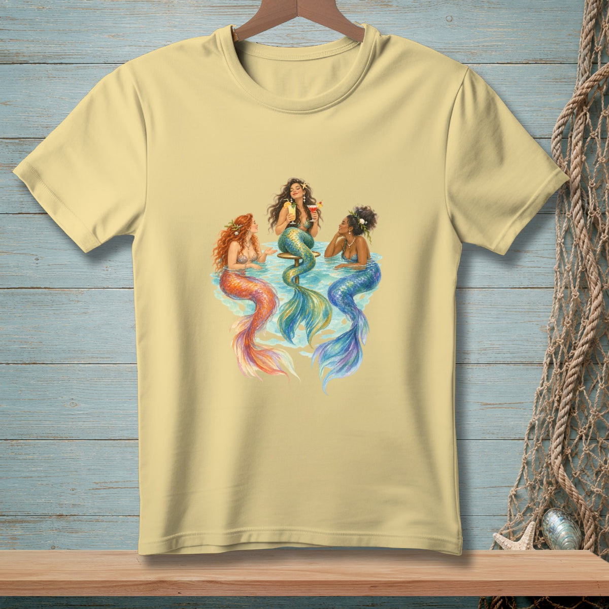 Three mermaids with colorful tails sit and drink cocktails together.