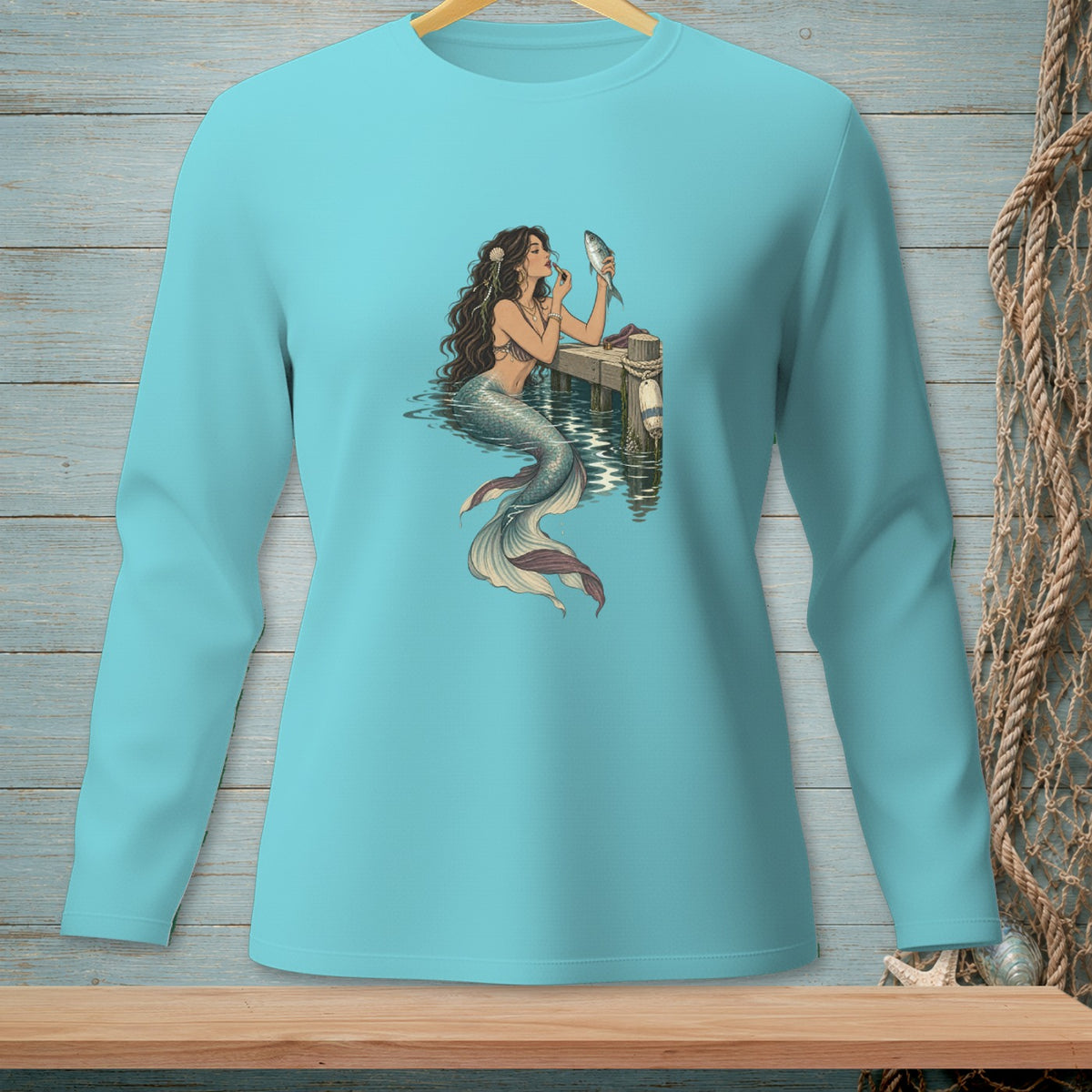 Teal long-sleeve shirt with a mermaid applying makeup to a fish.