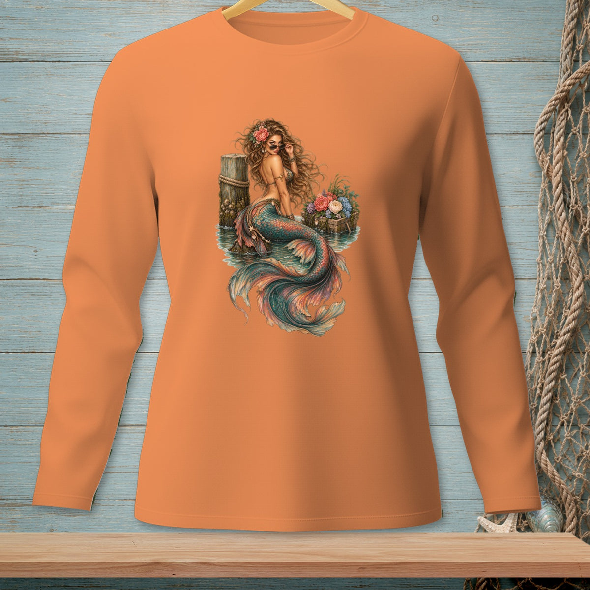 Orange long-sleeve shirt with a watercolor-style mermaid graphic and floral accents.