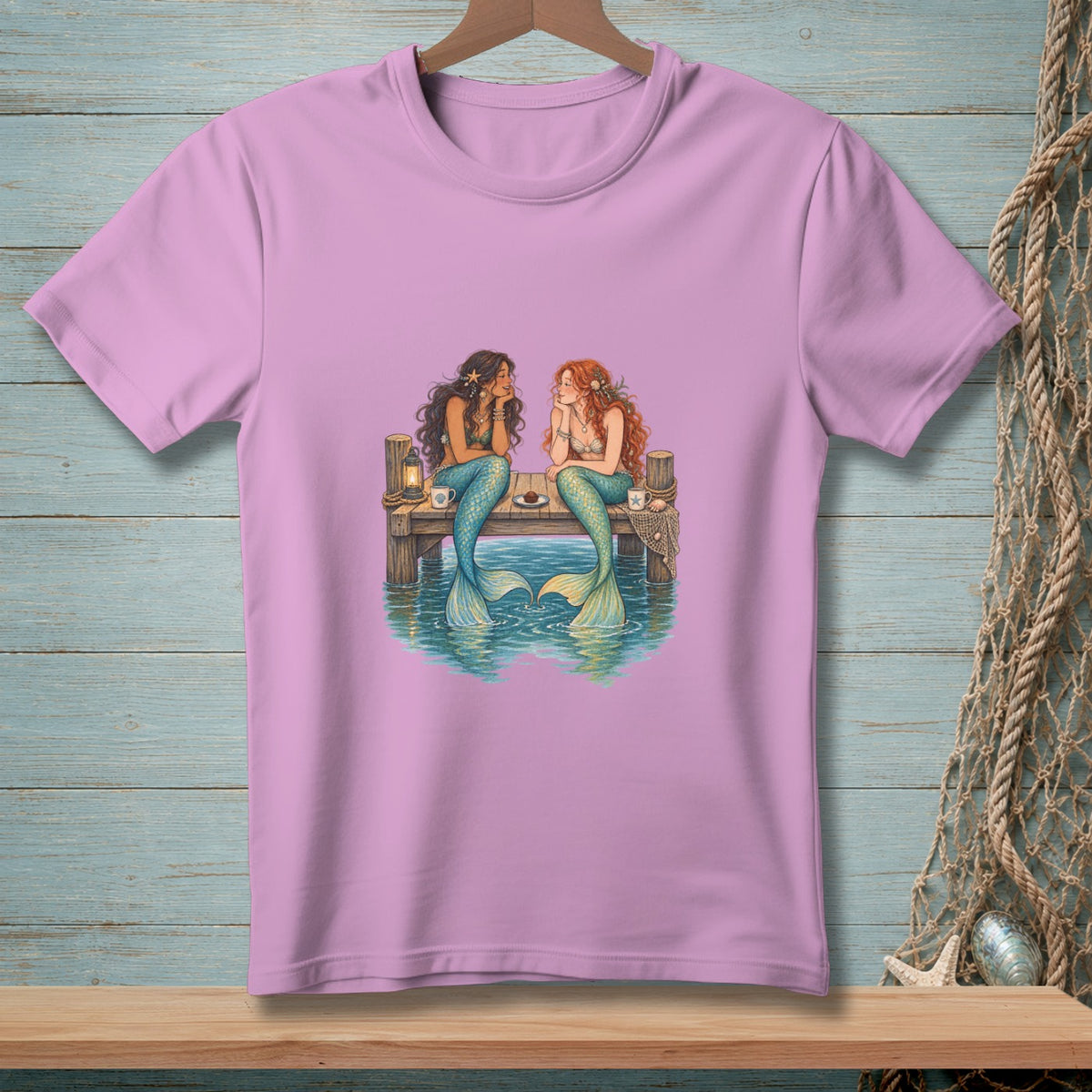 Two mermaids sit on a dock, talking, with the ocean below them.