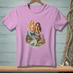Two mermaids sit on a rock by the water, one holding a pearl.