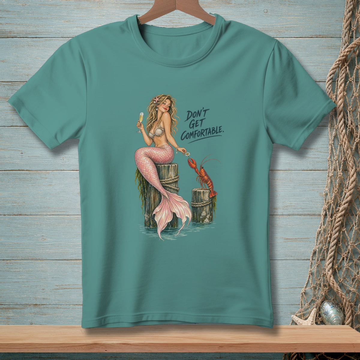 Mermaid with lobster and text "DON'T GET COMFORTABLE." on teal shirt.