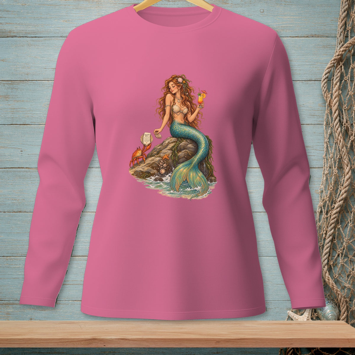 Pink long-sleeve shirt with a mermaid, crab, and drink graphic on a rock.