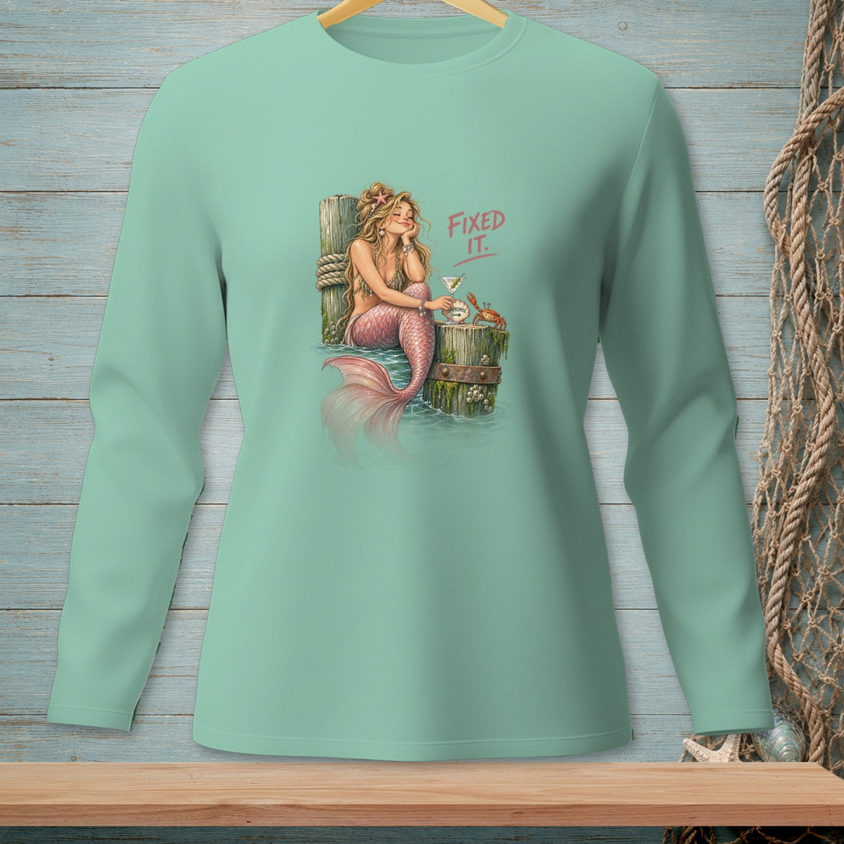 Mermaid with pink tail relaxing by a post with a drink and crab, text "FIXED IT."