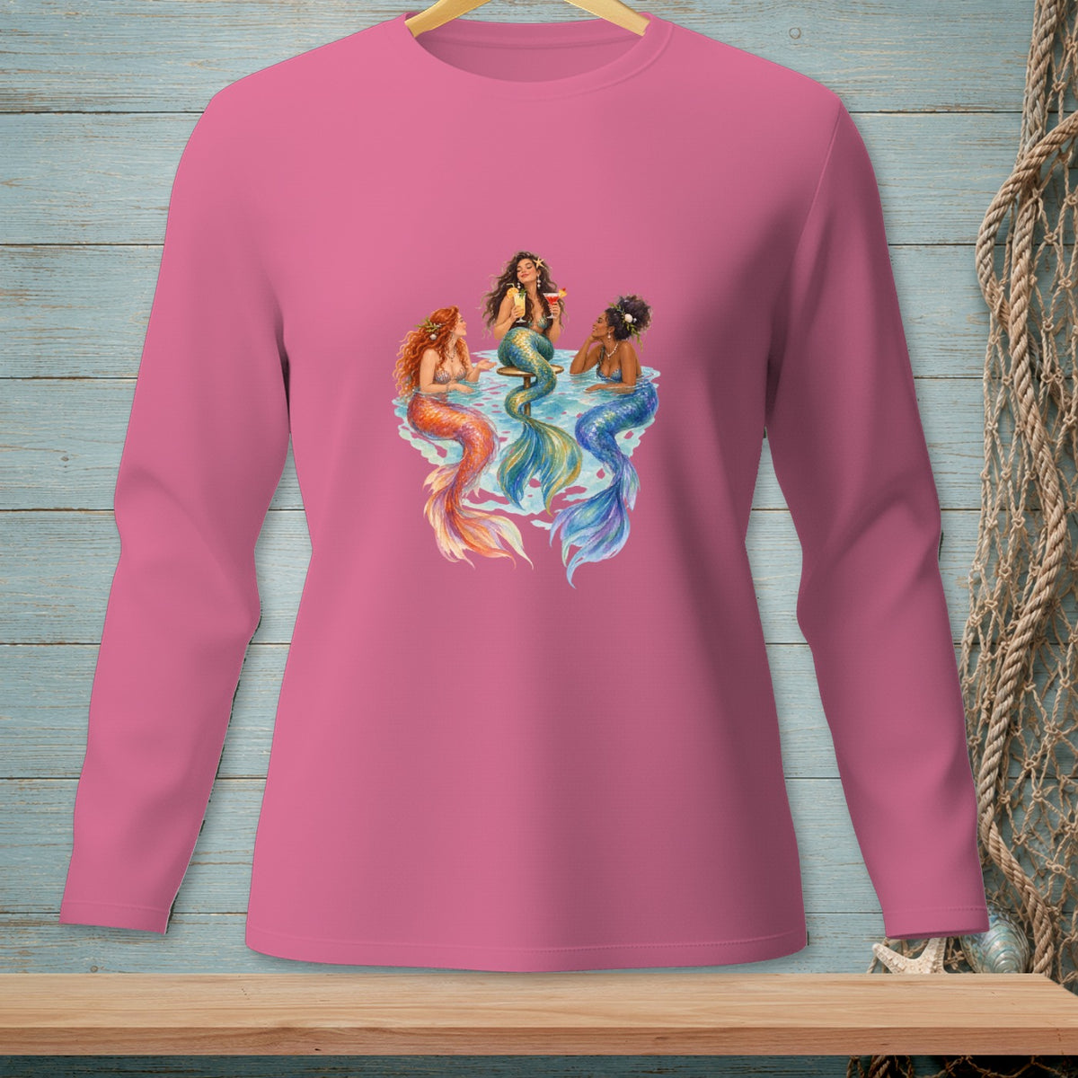 Three mermaids with colorful tails sit in water, holding drinks.
