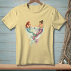 Two mermaids with colorful tails sit at a table in water, serving cake.