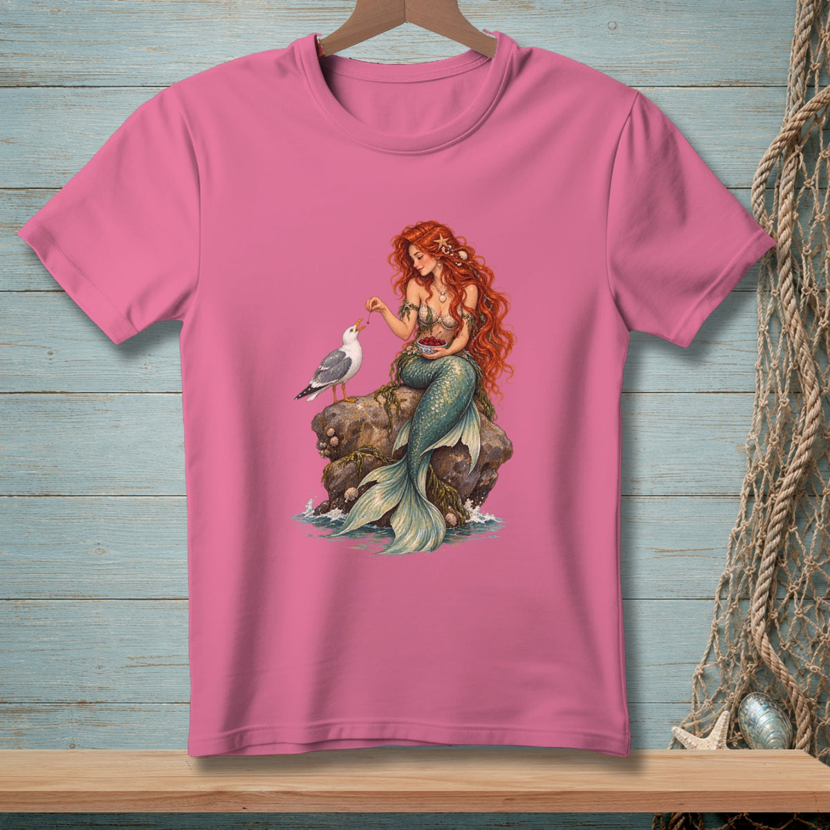 Pink t-shirt featuring a mermaid feeding a seagull on a rock.