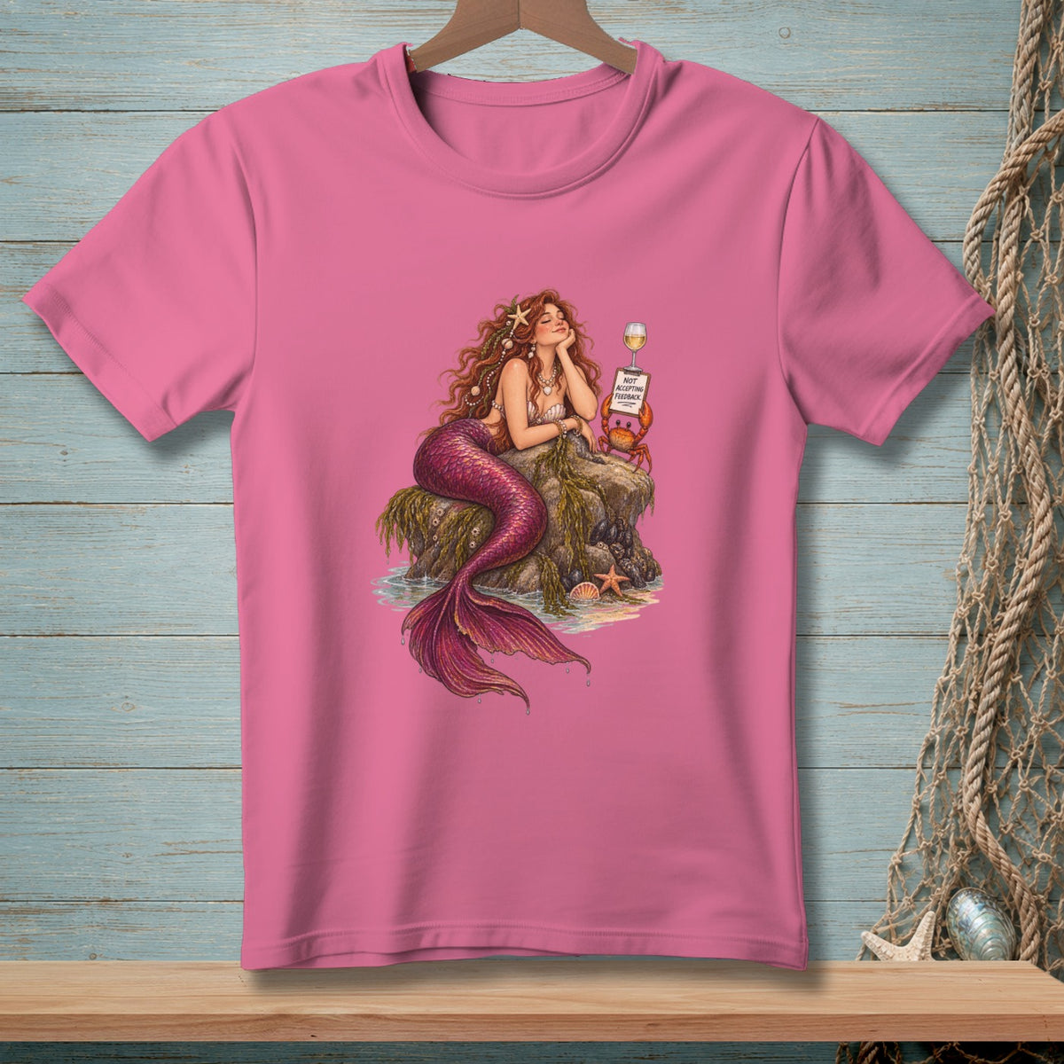 Pink t-shirt featuring a mermaid relaxing on rocks with a crab holding a "Not Accepting Feedback" sign.