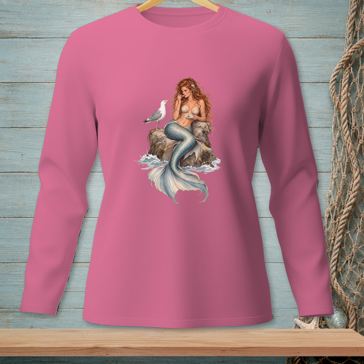 Pink long sleeve shirt with a mermaid and seagull on a rock graphic.