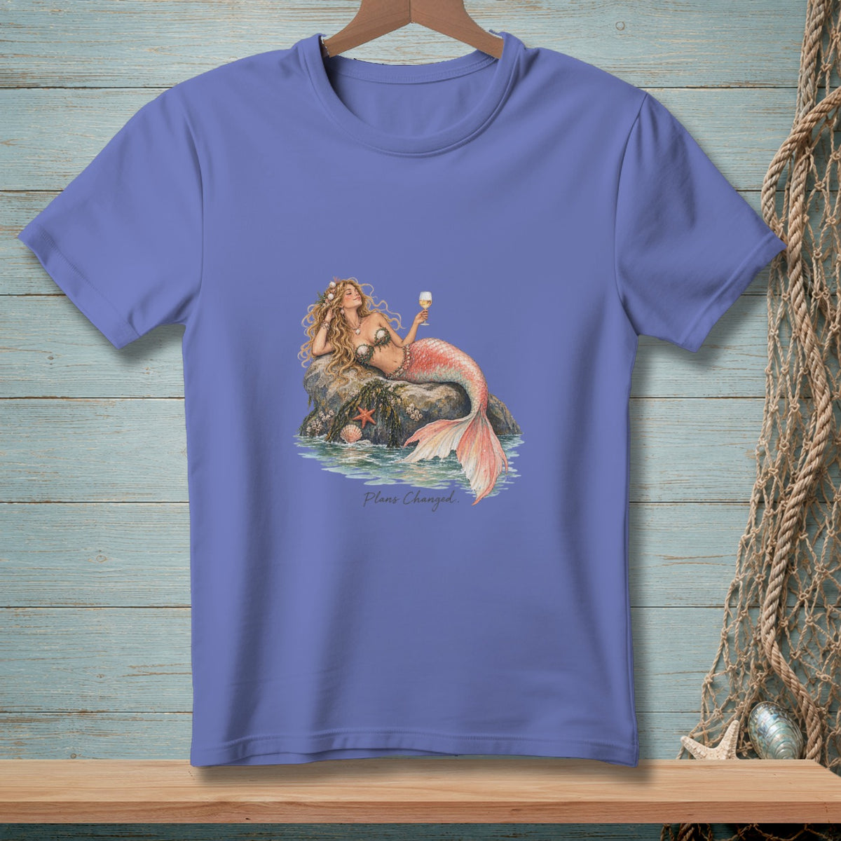 Purple t-shirt with illustration of a mermaid relaxing on a rock holding a drink.