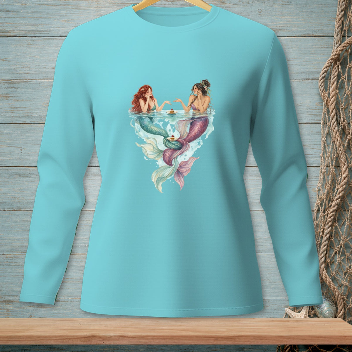 Aqua long sleeve shirt with two mermaids sharing cake at the water's surface.