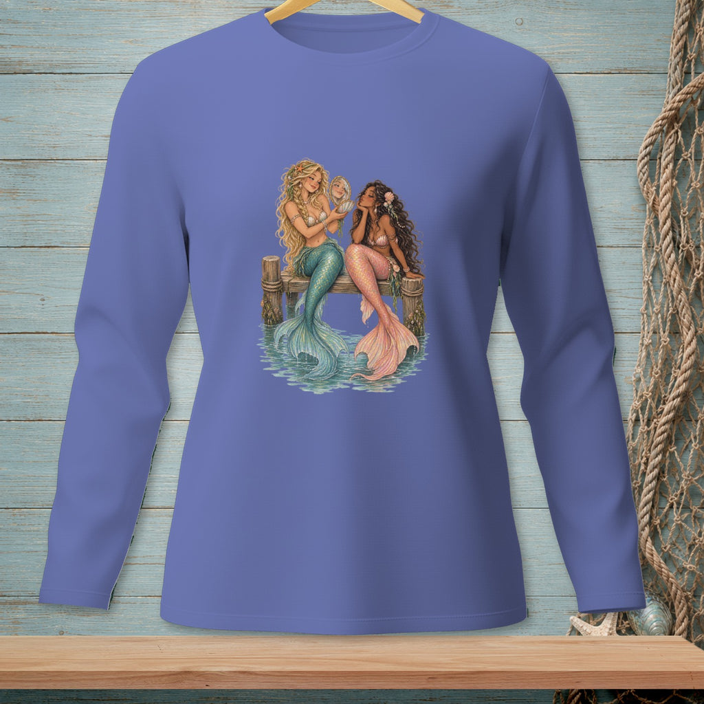 Two mermaids with colorful tails sit on a wooden dock looking at a shell.