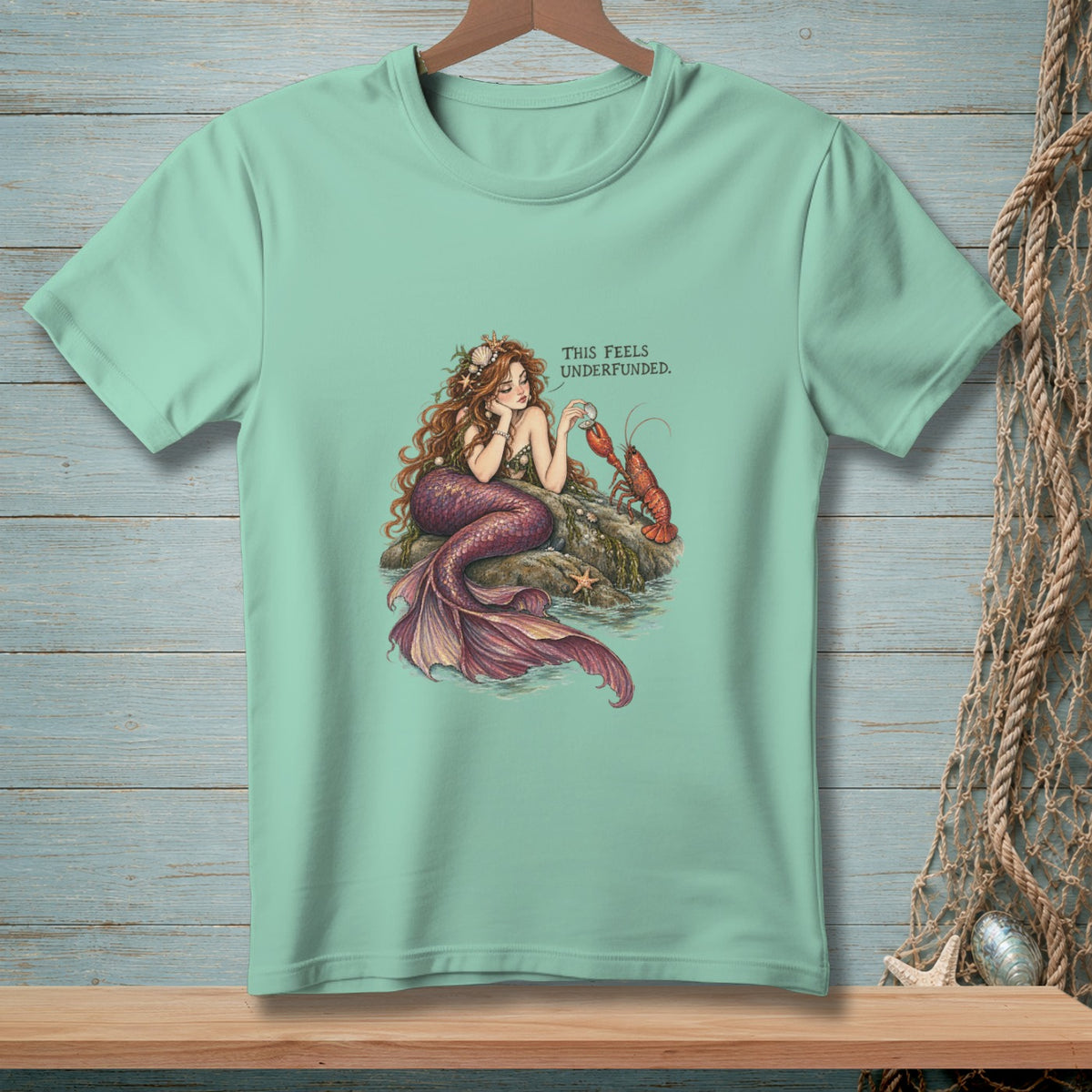 Mermaid with lobster on rock with text "THIS FEELS UNDERFUNDED."