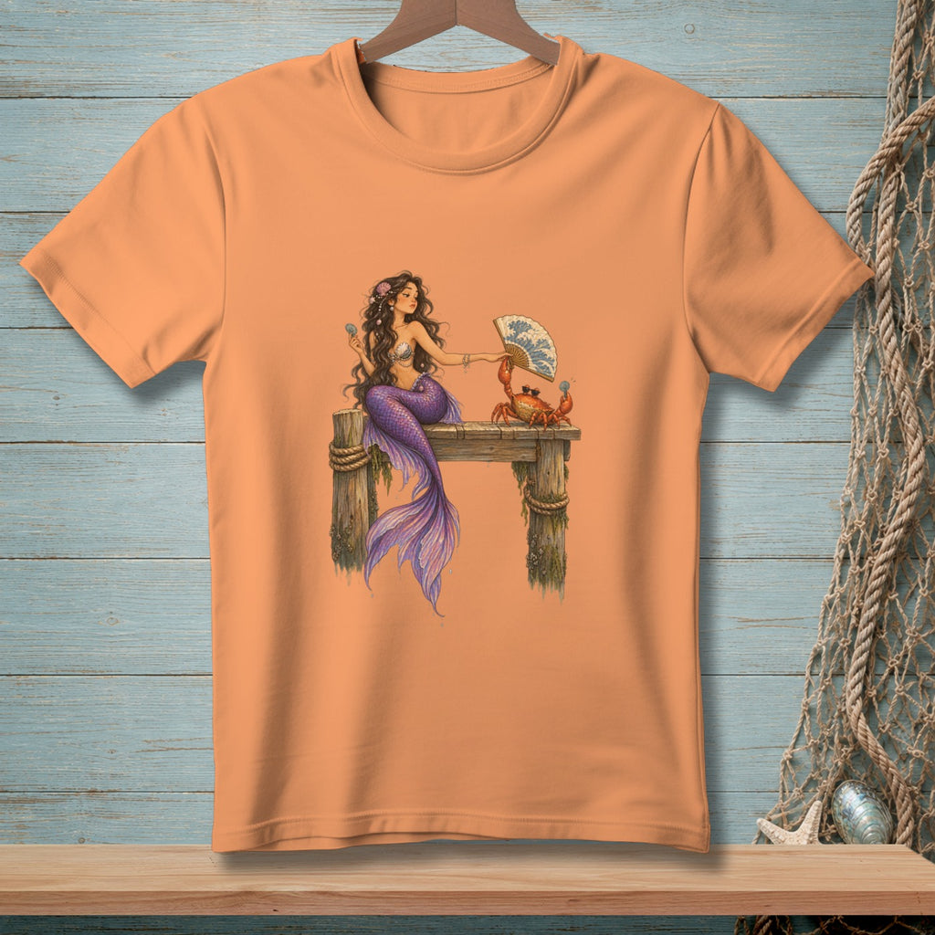 Peach t-shirt with a mermaid and crab design on a wooden pier.