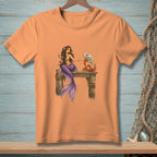 Peach t-shirt with a mermaid and crab design on a wooden pier.