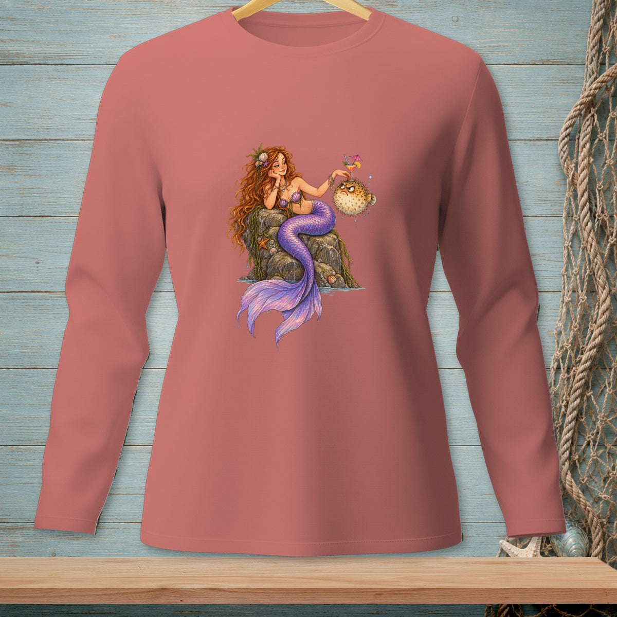 Mermaid with purple tail, holding cocktail with grumpy pufferfish, on pink long-sleeve shirt.