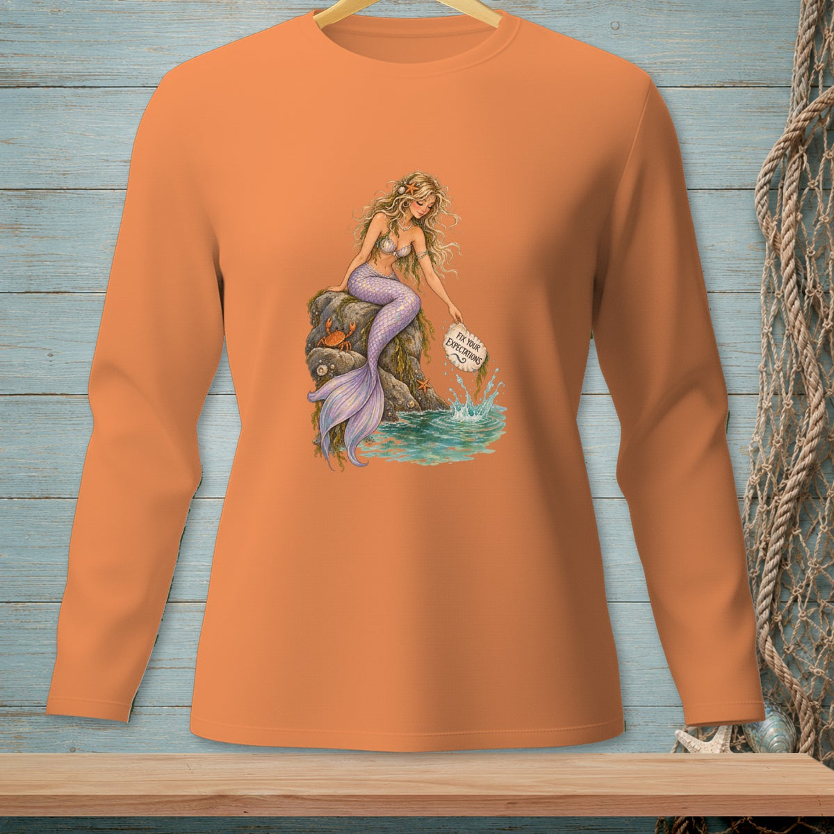 Orange long-sleeve shirt with a mermaid sitting on a rock, holding a sign that says "Fix Your Expectations."