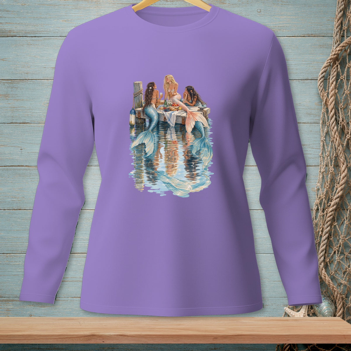 Three mermaids have a picnic on a dock reflected in the water.