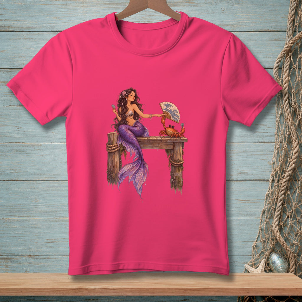 Mermaid and crab with a fan on a pier graphic on a pink t-shirt.