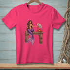 Mermaid and crab with a fan on a pier graphic on a pink t-shirt.