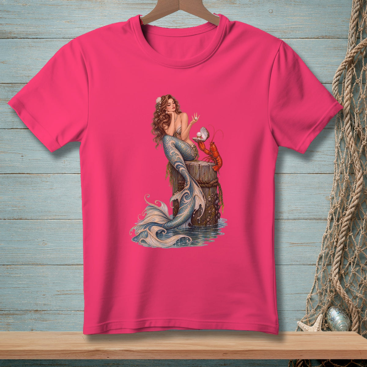 Pink t-shirt with a detailed print of a mermaid and lobster sitting on a weathered post.