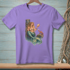 Purple t-shirt with a mermaid holding a shell next to a crab on a rock.