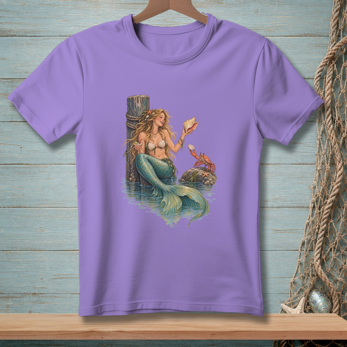 Purple t-shirt with a mermaid holding a shell next to a crab on a rock.