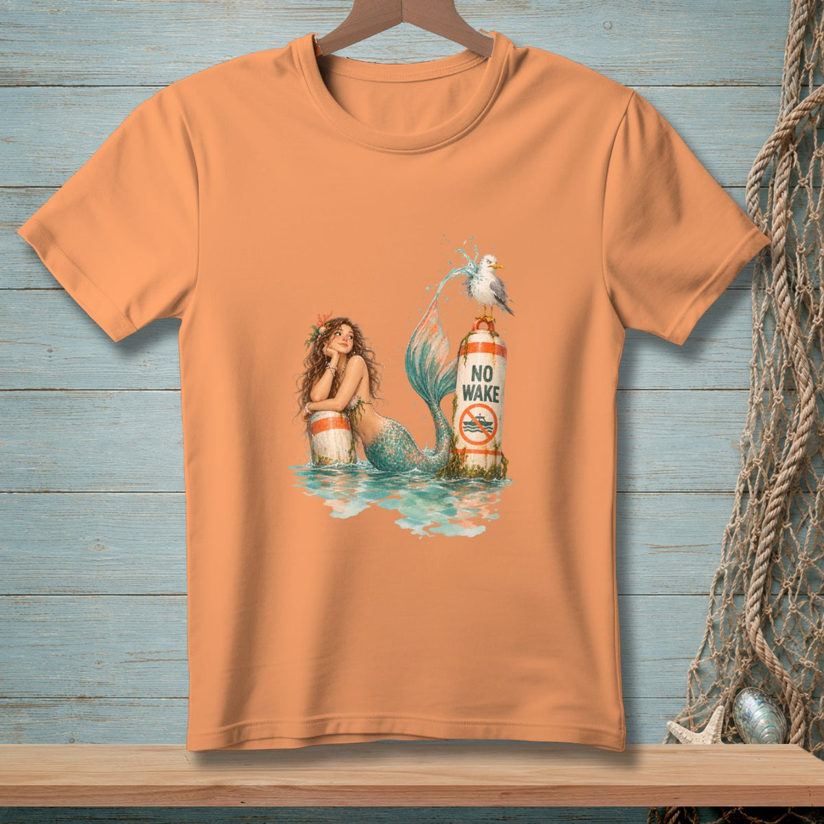 Peach t-shirt with a mermaid, seagull, and "NO WAKE" sign illustration.