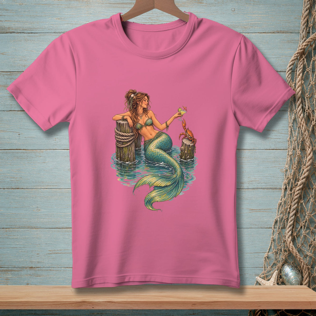 Pink t-shirt with illustration of a mermaid holding a drink near a crab.