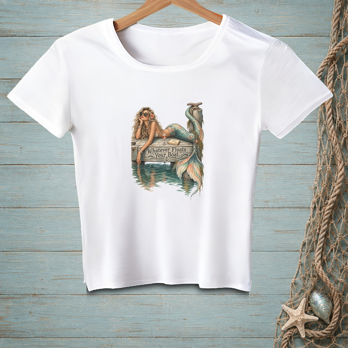 White t-shirt with a graphic of a mermaid on a dock, reading "Whatever Floats Your Boat."