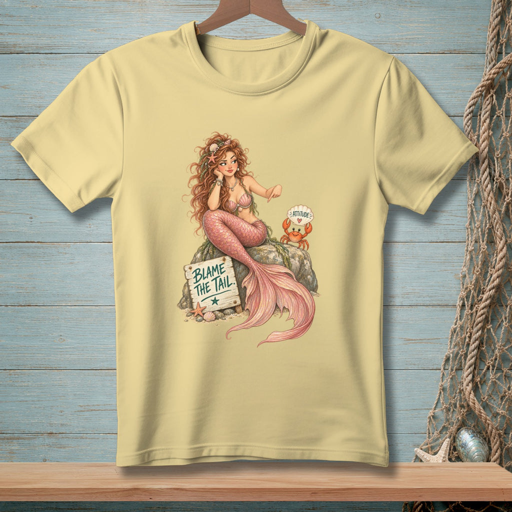 Mermaid with pink tail and crab sits on rock with "Blame the Tail" sign.