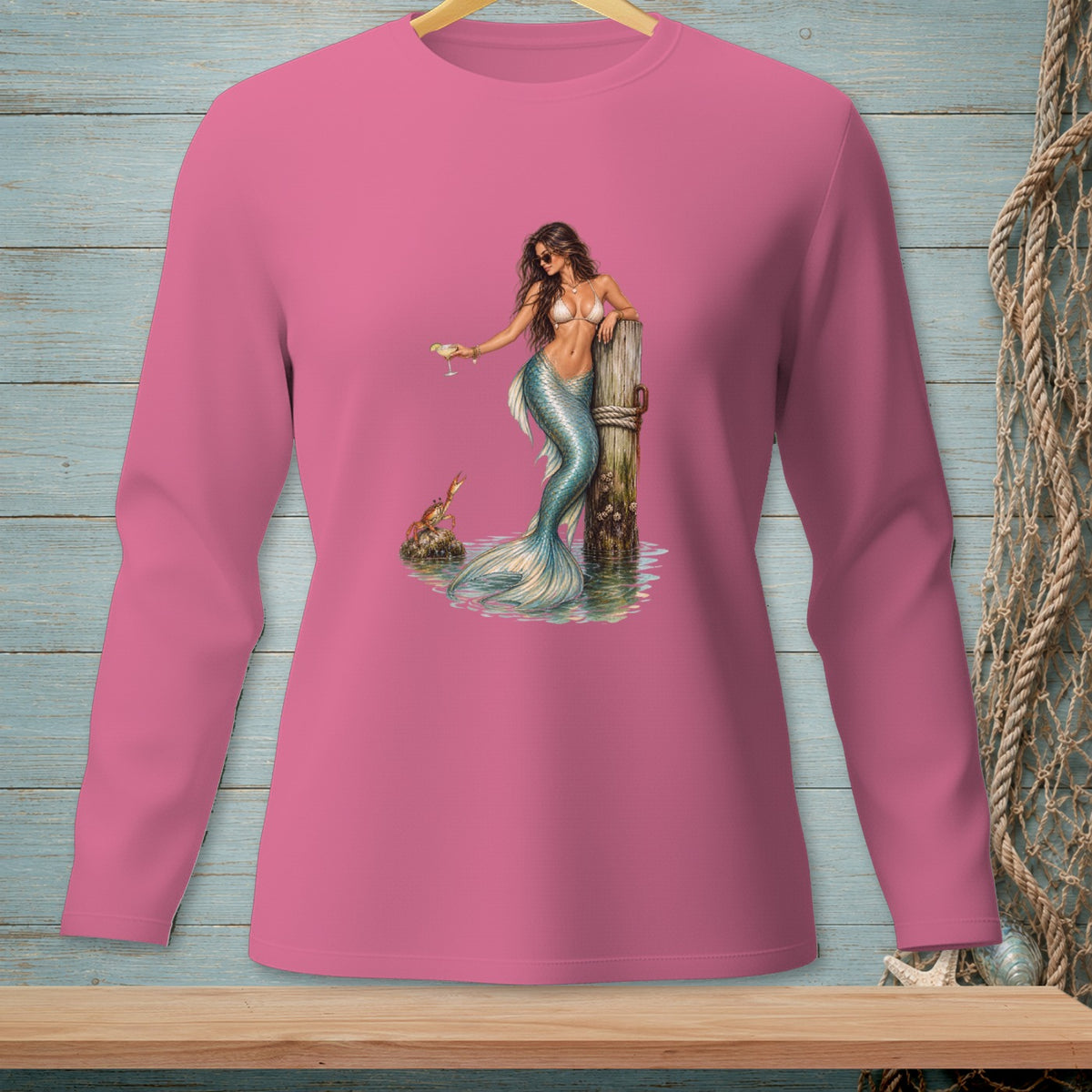 Pink long-sleeve shirt with a mermaid holding a drink by a dock.