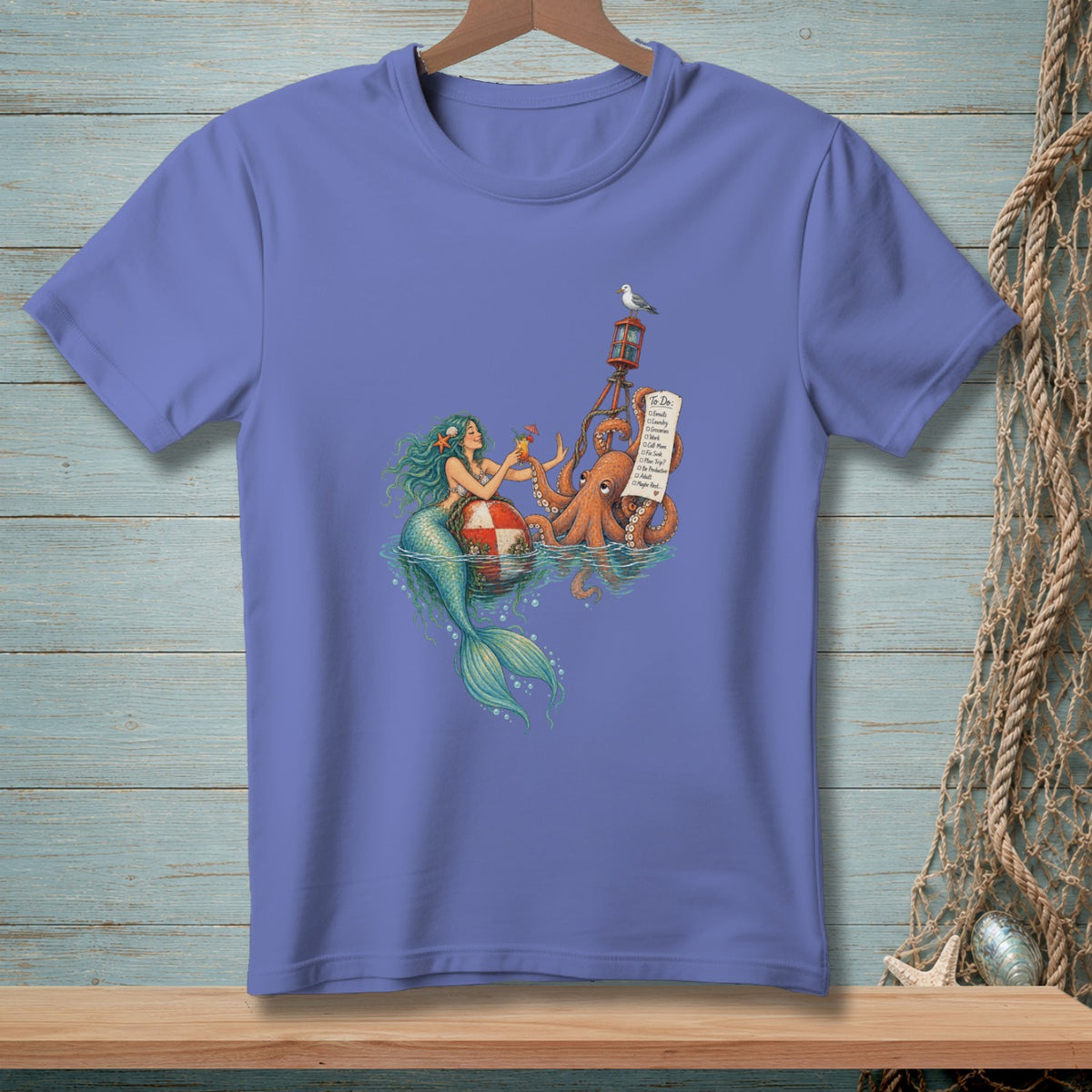 A periwinkle t-shirt featuring an illustration of a mermaid, an octopus holding a to-do list, and a lighthouse.