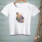 A white t-shirt on a wooden background features a graphic of a mermaid with a face mask relaxing on a rock.
