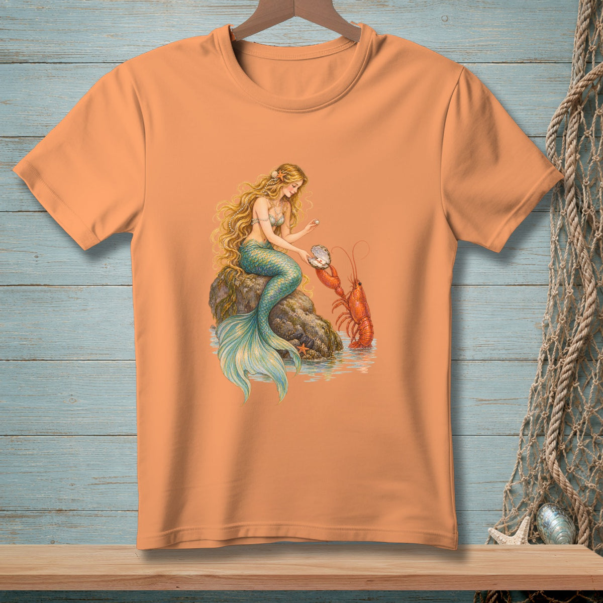 Peach t-shirt with mermaid and lobster art, featuring a mermaid sitting on a rock with a pearl.