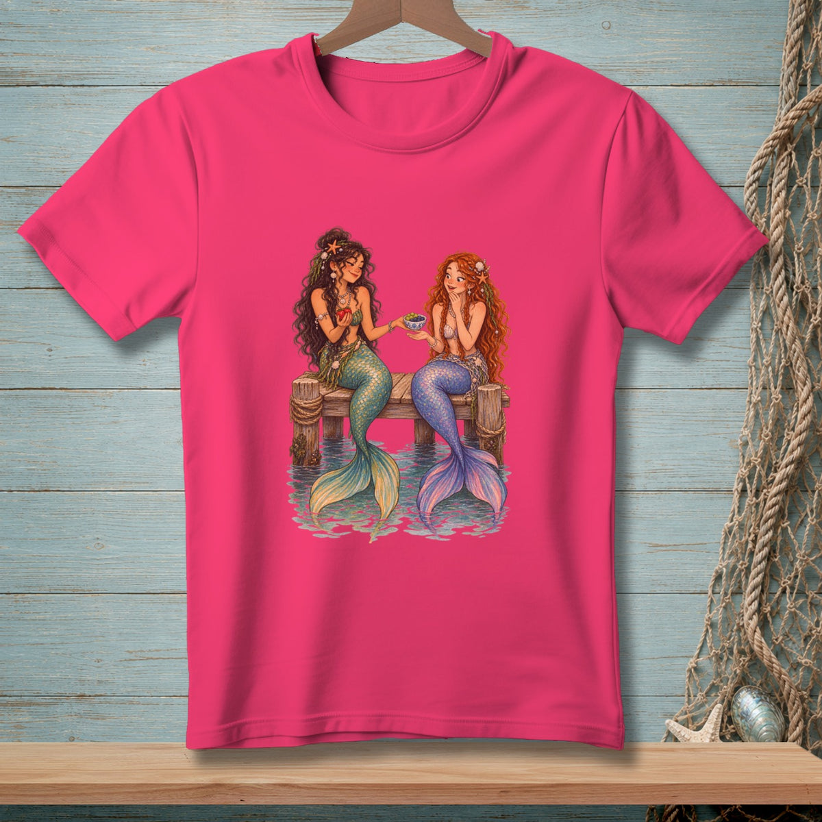 Two mermaids with colorful tails sit on a wooden dock sharing food.