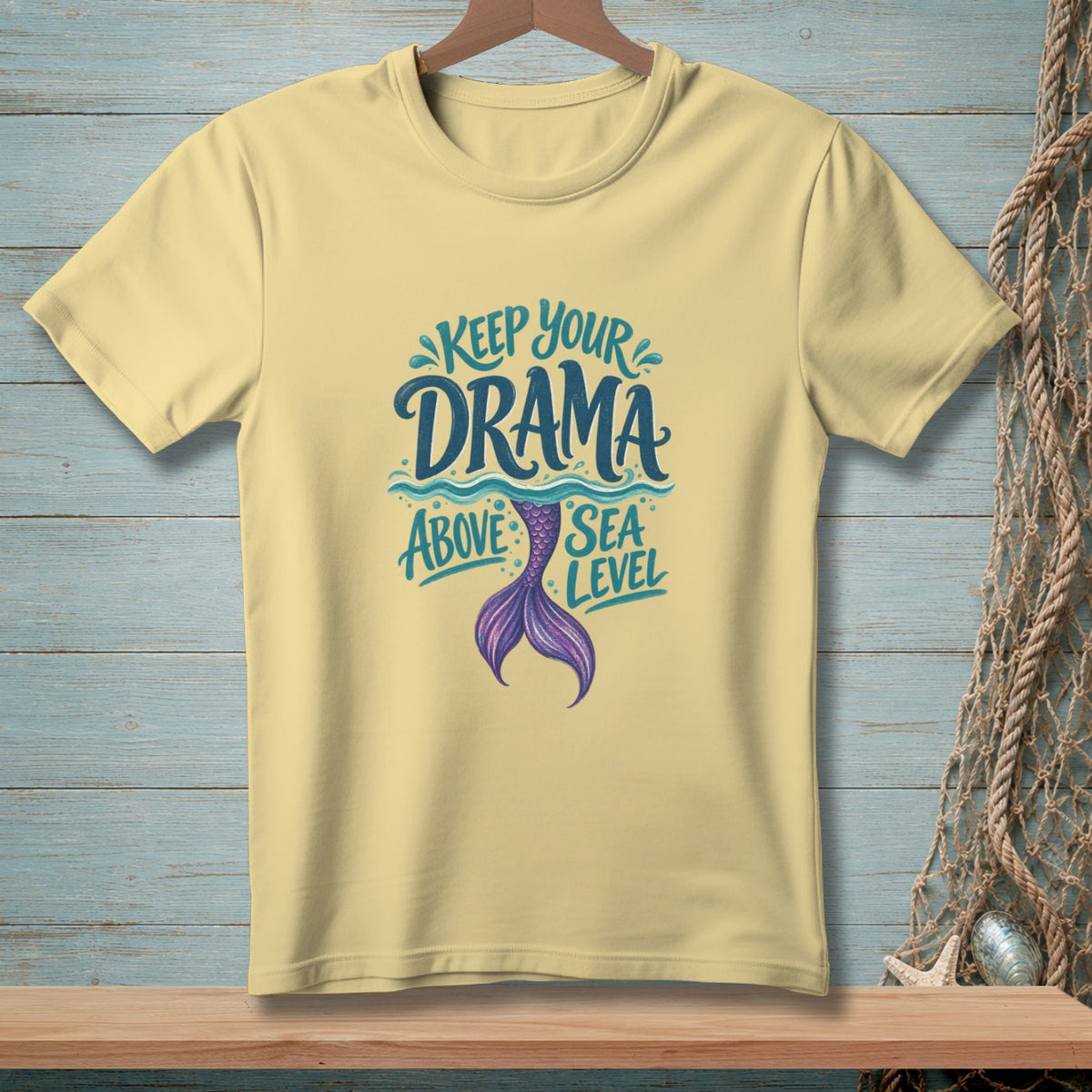 Pale yellow t-shirt with "Keep Your Drama Above Sea Level" text and mermaid tail graphic.