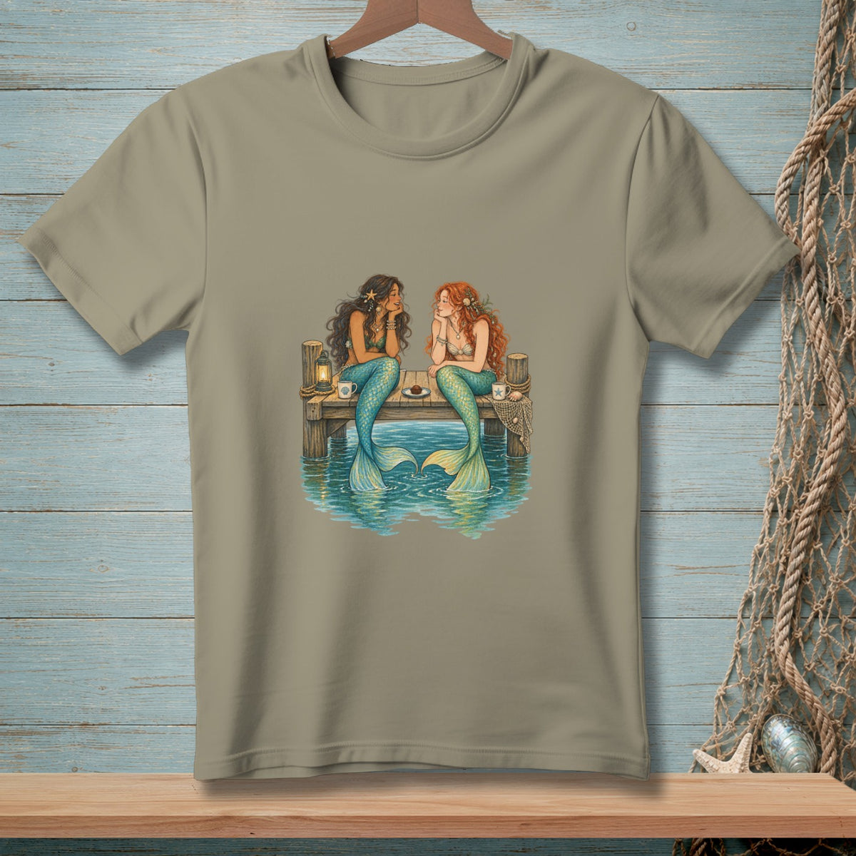 Two mermaids sit on a dock, talking with drinks and food.