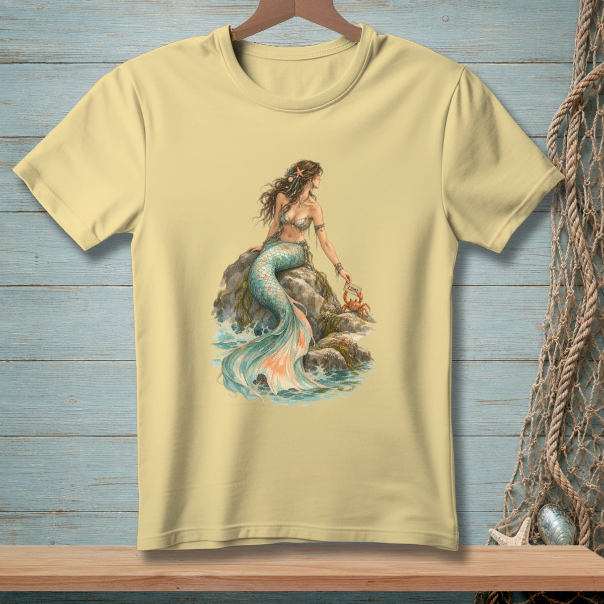 Pale yellow t-shirt with a watercolor illustration of a mermaid and a crab.