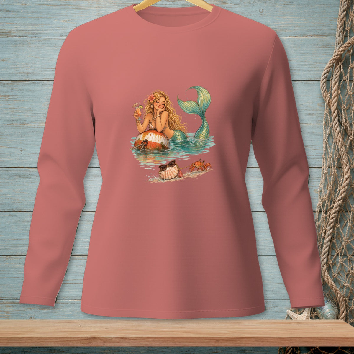 Mermaid on a buoy with a drink, crabs, and shells on a beach.